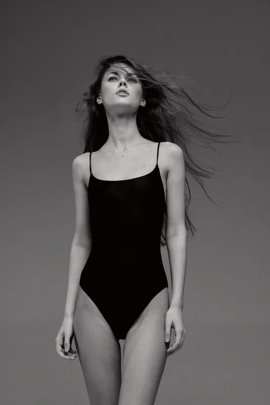 Black and white portrait of a woman in a black bodysuit with flowing hair and a confident expression