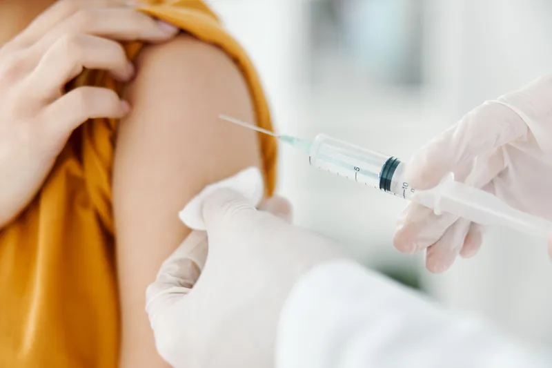 Врач делает инъекцию вакцины в плечо пациента в медицинской маске в больнице во время эпидемии