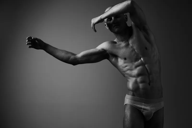 Athletic man posing in black and white, showcasing toned physique and strong emotions. A dramatic and artistic expression of strength and vulnerability.