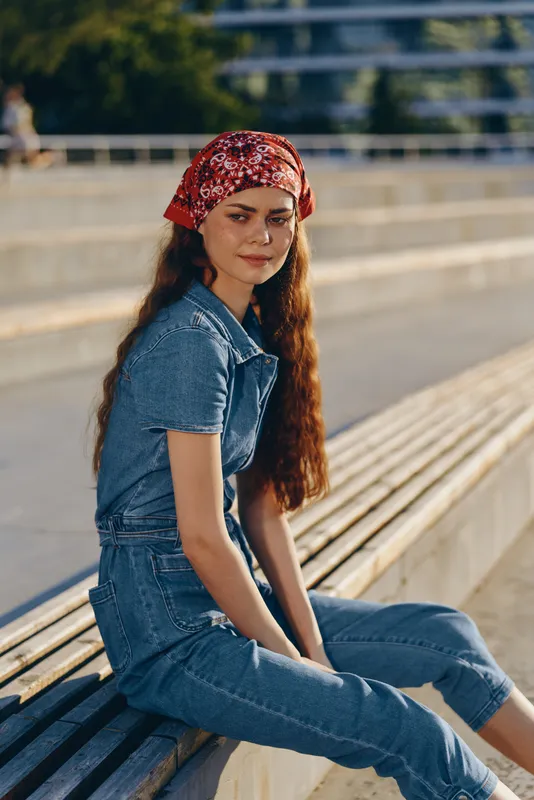 young woman sitting outdoors wearing denim clothes and red bandana, natural light, relaxed mood, warm sunlight, casual style, urban background
