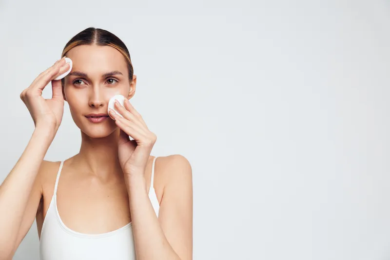 Young woman with clear skin uses cotton pads to cleanse her face daily skincare routine isolated on white background for beauty and health concept
