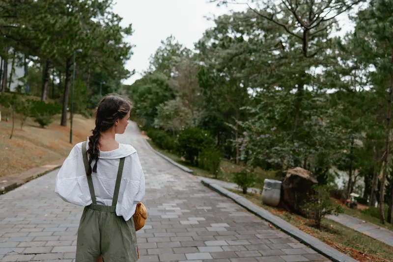 Young woman in nature wearing casual summer outfit, enjoying a walk on a peaceful path surrounded by greenery and trees, conveying a sense of calmness and serenity