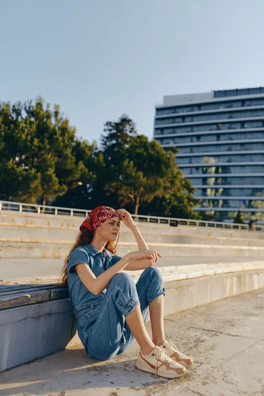 Lifestyle woman in modern boho-western denim street style sitting outdoors with relaxed pose and film color tones under natural daylight urban background.