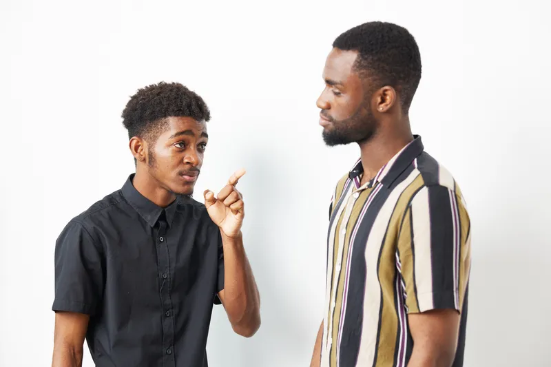Two African American men in a casual conversation, one gesturing animatedly. Their expressions reveal engaging dialogue and mutual interest, creating a vibrant interaction.