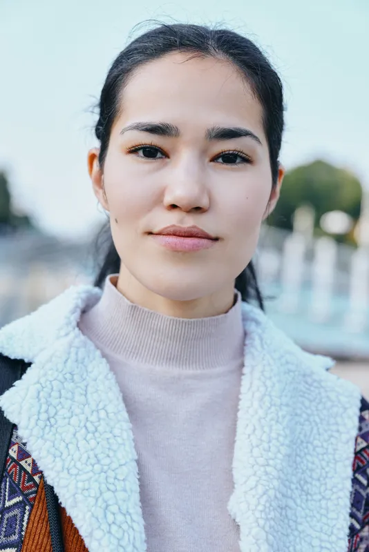 Woman wearing a cozy fleece coat outdoors, calm expression, soft natural light, shallow depth of field, urban background, cool tones, casual fashion mood, clean background, modern style, approachable