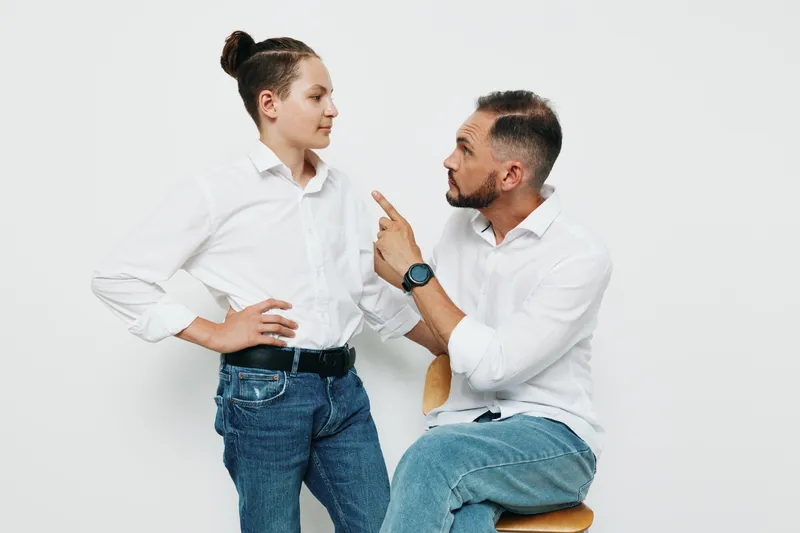 A confident professional man in a white shirt interacts with a young colleague against an isolated white background, portraying leadership, guidance, and focused collaboration.