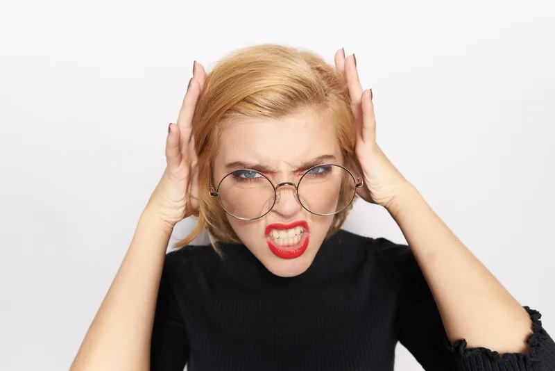 Милая блондинка в очках с ярким макияжем, в чёрной куртке, обрезка на светлом фоне, эмоции