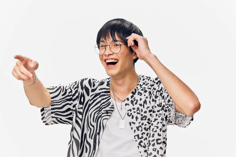 cheerful young man laughing and pointing, wearing patterned shirt and glasses, isolated on white background, joyful expression