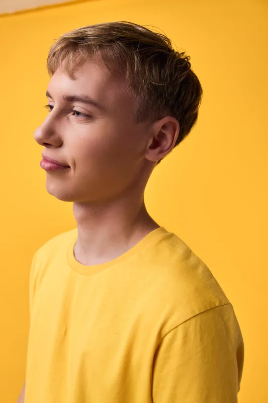 Man wearing a yellow tee against a bright yellow backdrop, calm expression, casual style, fashion and lifestyle photo emphasizing warmth, positivity, and sunny mood
