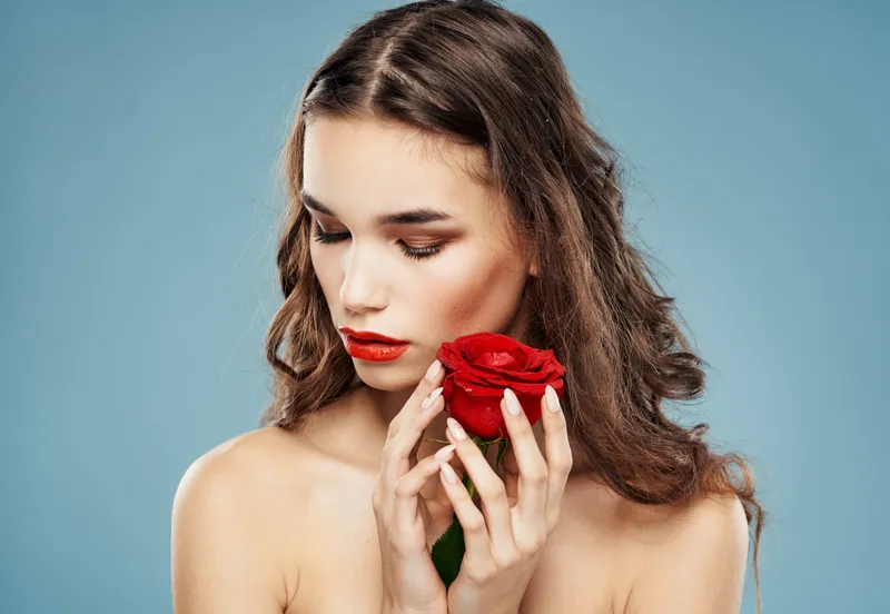Женщина-модель с красной розой возле лица на синем фоне