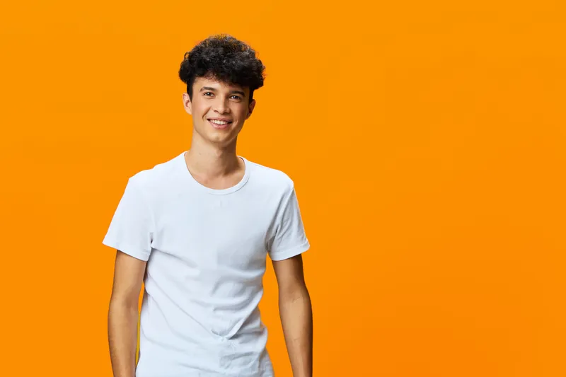 smiling young man wearing casual white t-shirt stands against vibrant orange background with relaxed posture and cheerful expression, studio portrait