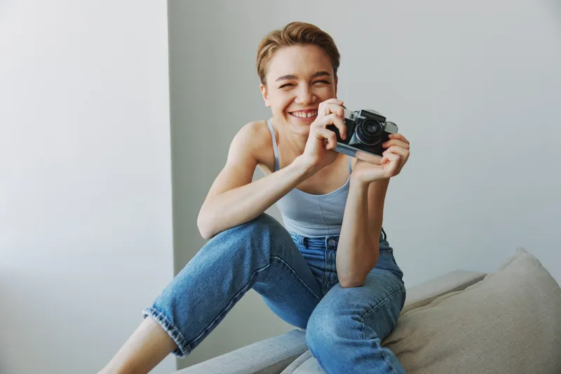 Женщина-фотограф снимает в студии на старую плёночную камеру, сидя на диване дома