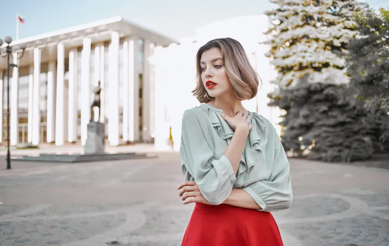 Женщина в рубашке и юбке прогуливается по центральным улицам города на фоне высотных зданий
