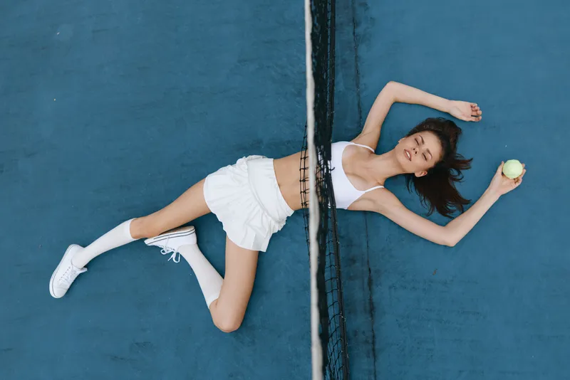 Young athletic woman enjoying summer tennis, relaxation and sport, wearing a white sporty outfit and smiling on the court with a yellow tennis ball