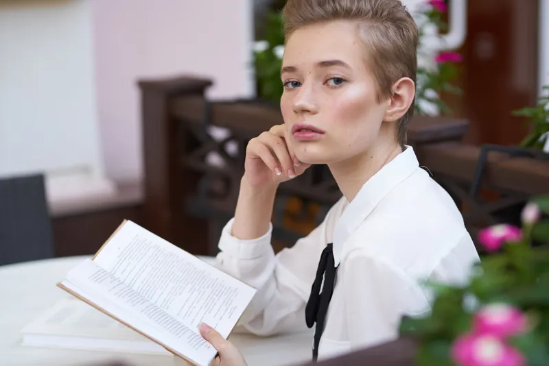 Студент с книгой в руках на открытом воздухе отдыхает, весело прогуливаясь по городу