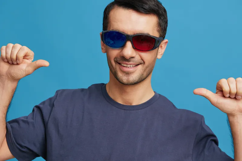 Портрет мужчины в синей футболке и 3D-очках, развлекающегося жестами рук, кадр обрезан