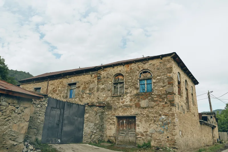 Rural rustic stone building with weathered facade and wooden doors in a quiet countryside setting, showcasing aging architecture, textured walls, and a calm, timeless atmosphere across a simple rural