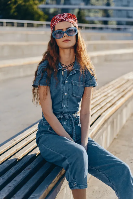 lifestyle woman in modern boho-western denim street style wearing sunglasses and bandana with film color effect, relaxed outdoor urban fashion vibe