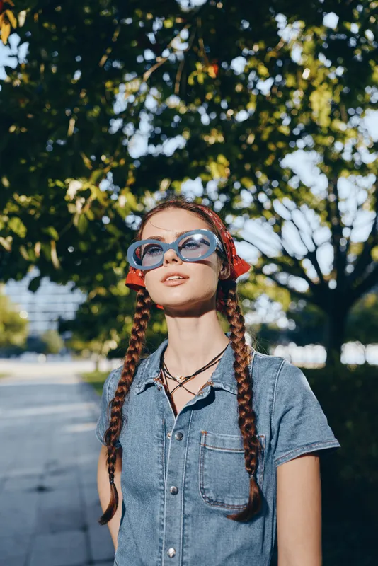 Lifestyle woman in modern boho-western denim street style wearing large sunglasses and braided hair outdoors with a film color effect under natural sunlight.