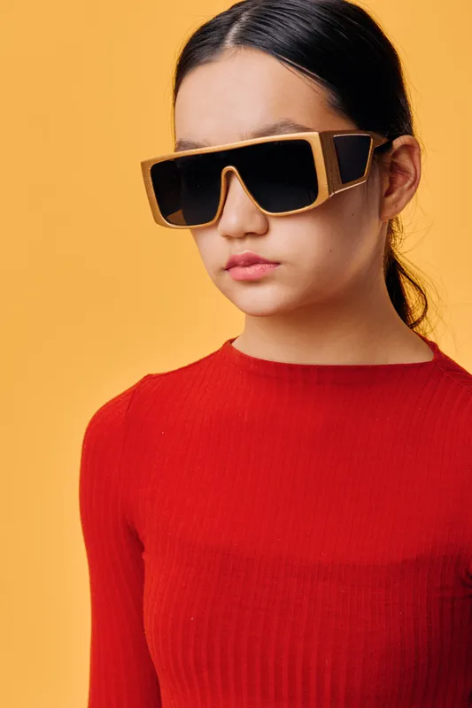 Teenage girl wearing large stylish sunglasses and red sweater with straight hair against yellow background for fashion look, beauty, youth and modern style portrait.