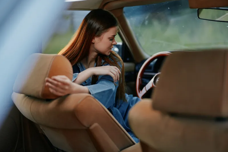Young woman with long hair sitting in a vintage car, reflecting on life with a serene expression, dressed casually in denim, capturing a nostalgic moment.