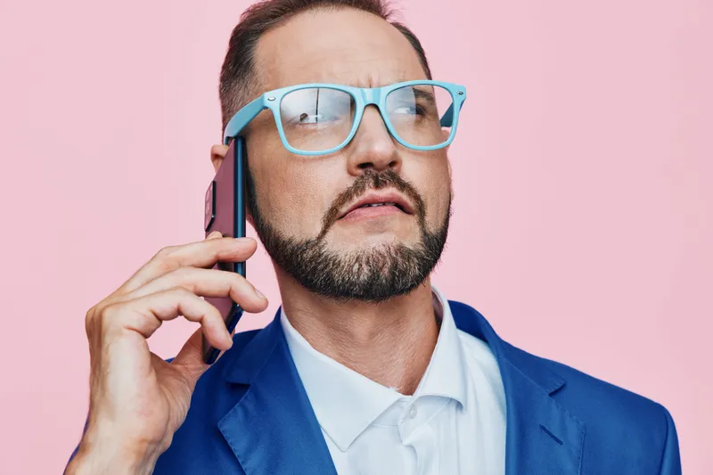 A focused business professional speaks on a mobile phone, isolated on a solid colored backdrop. The scene conveys confident, thoughtful emotion and a calm, strategic mindset.