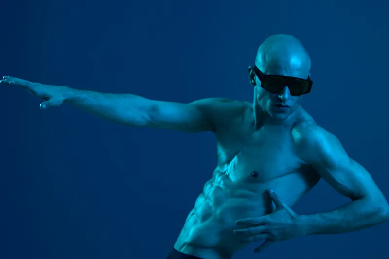 Athletic man striking a dynamic pose, showcasing toned muscles against a blue background with dramatic lighting. A captivating black and white composition.