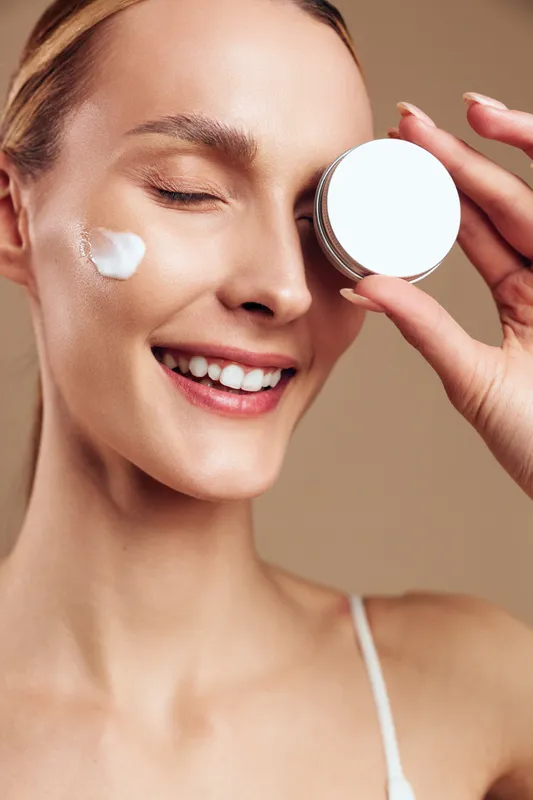 Woman skincare facial cream moisturizer beauty mirror smile treatment spa, close up portrait, woman applies eye cream with fingers, eyes closed, soft studio light