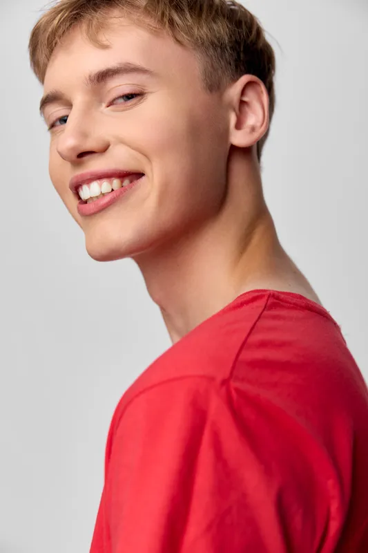 Smiling man, red shirt, young man, positive expression in studio lighting, casual pose, bright mood, clean background, friendly vibe with welcoming charm for stock use