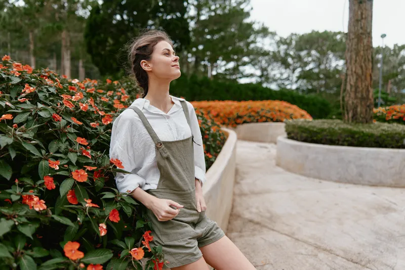 Young woman in casual outfit enjoying nature among colorful flowers, exuding tranquility and confidence during a sunny season outdoors