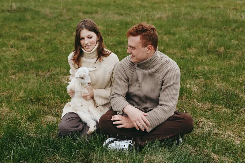 A couple sits on a grassy field with a small dog, enjoying a relaxed outdoor moment. A candid lifestyle scene showing companionship, warmth, and casual togetherness in nature.