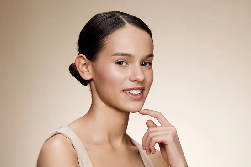 Young woman with a natural smile posing against a soft beige background, showcasing confidence and beauty