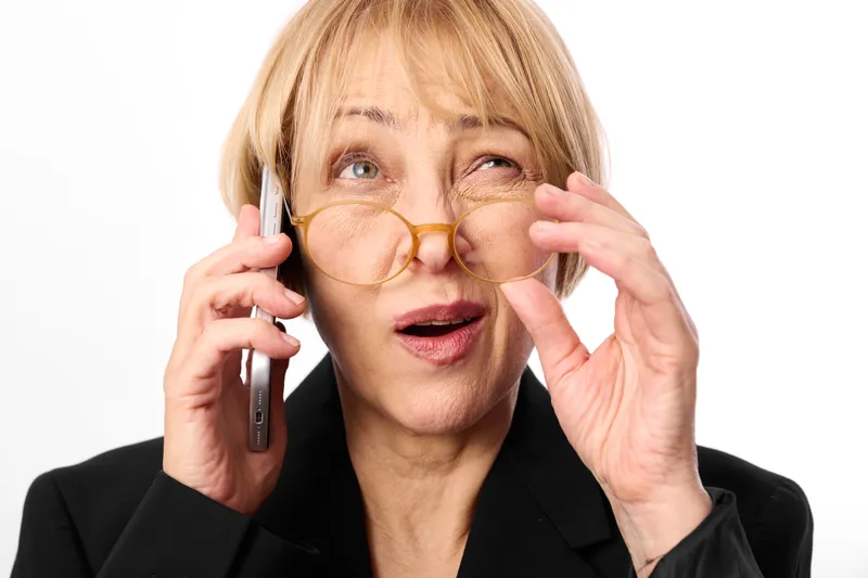 Senior woman holding eye patch on both eyes while talking on phone, close up on white background, skincare beauty routine, calm studio lighting, self care concept wellness