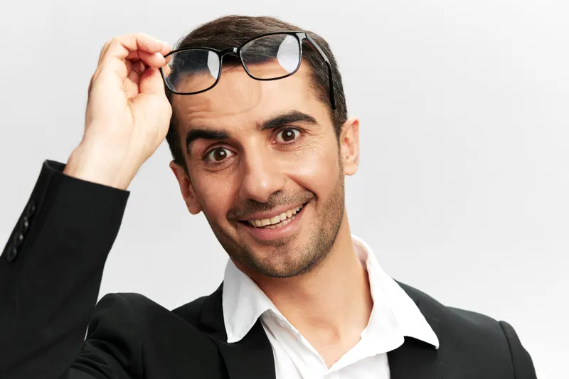 Весёлый мужчина в деловом костюме, крупным планом, в очках, кадр обрезан, светлый фон