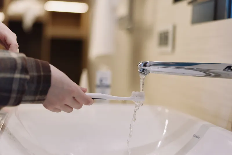 Toothbrush in hand, brushing under running water at a sink in a bright bathroom, highlighting hygiene and health through daily dental care.