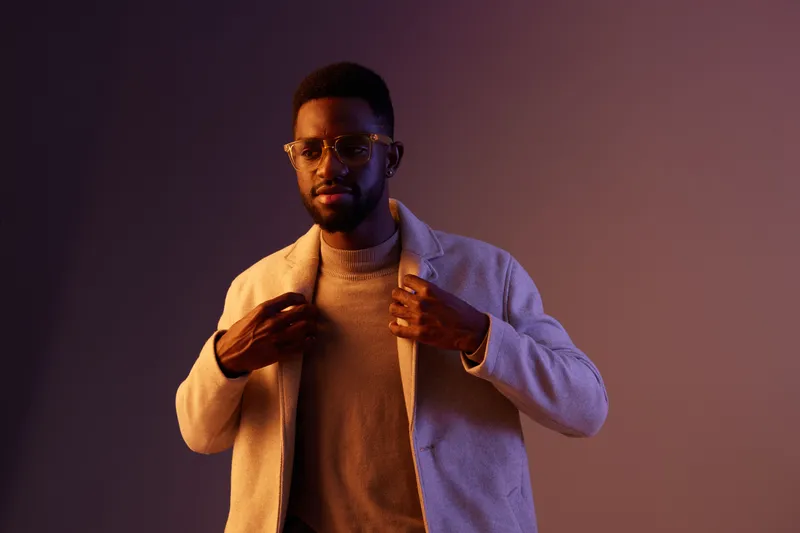 Stylish man adjusting his coat with confidence, showcasing modern fashion in warm tones and a soft gradient background, ideal for fashion and lifestyle themes