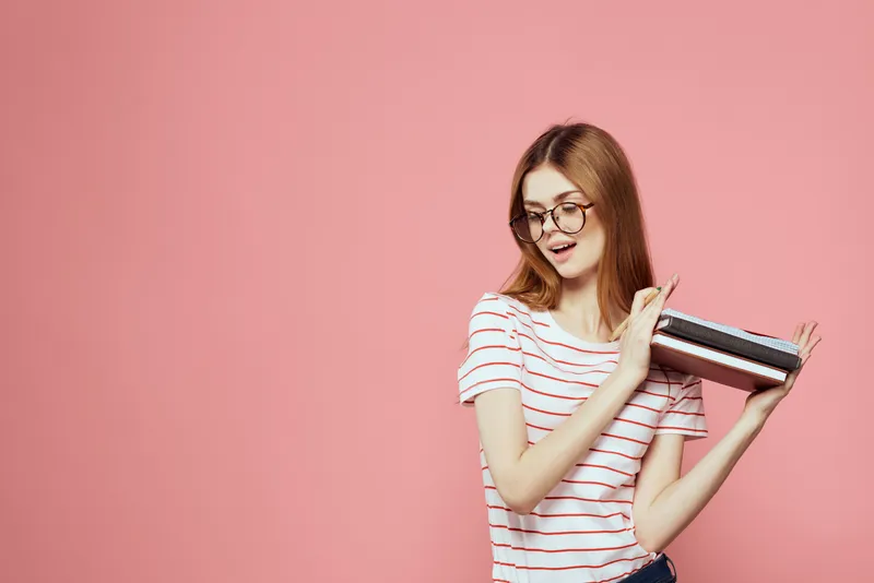 Молодая студентка с книгами на розовом фоне, в очках, крупный план лица