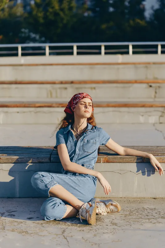 lifestyle woman in modern boho-western denim street style sits relaxed outdoors in warm sunlight with film color tones creating a nostalgic atmosphere