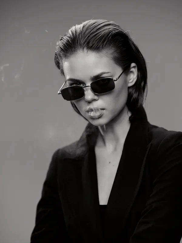 Stylish woman wearing sunglasses with slicked-back hair in a black and white portrait, showing a confident and edgy expression.