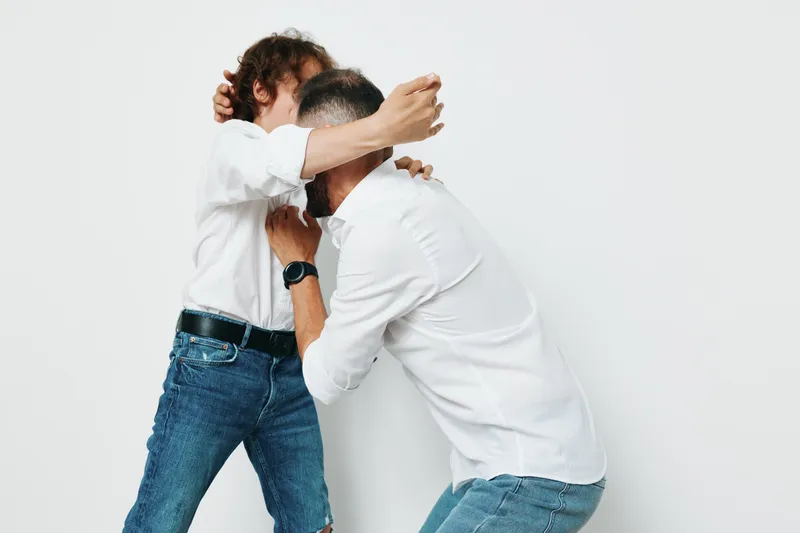 A professional business vibe with two men in white shirts embracing, captured against an isolated colored background, expressing emotion and teamwork in a dynamic corporate moment.