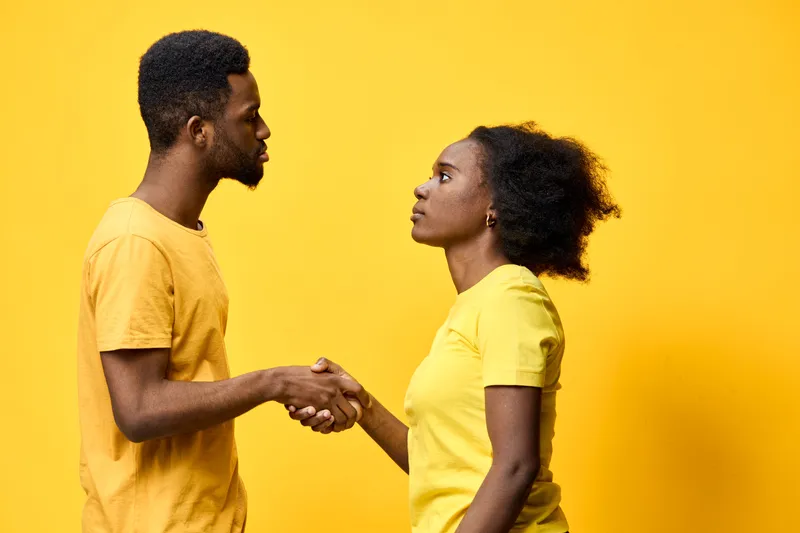 Two young adults shaking hands against a vibrant yellow background, showcasing partnership and collaboration, dressed in matching yellow attire, expressing determination and trust