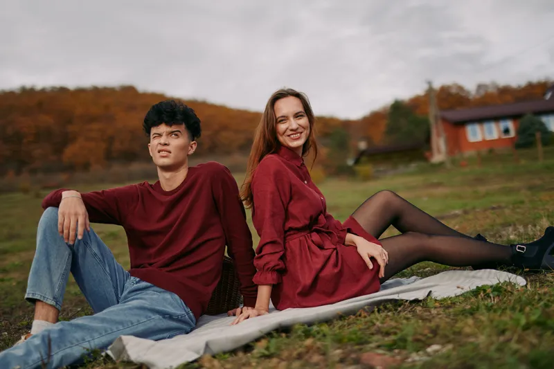 A candid outdoor portrait shows an authentic connection between two friends resting on a blanket in a park, autumn light, relaxed posture, and genuine smiles.