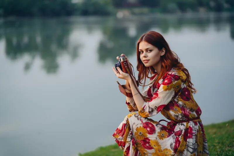 Симпатичная женщина с фотоаппаратом у озера на открытом воздухе, отдых