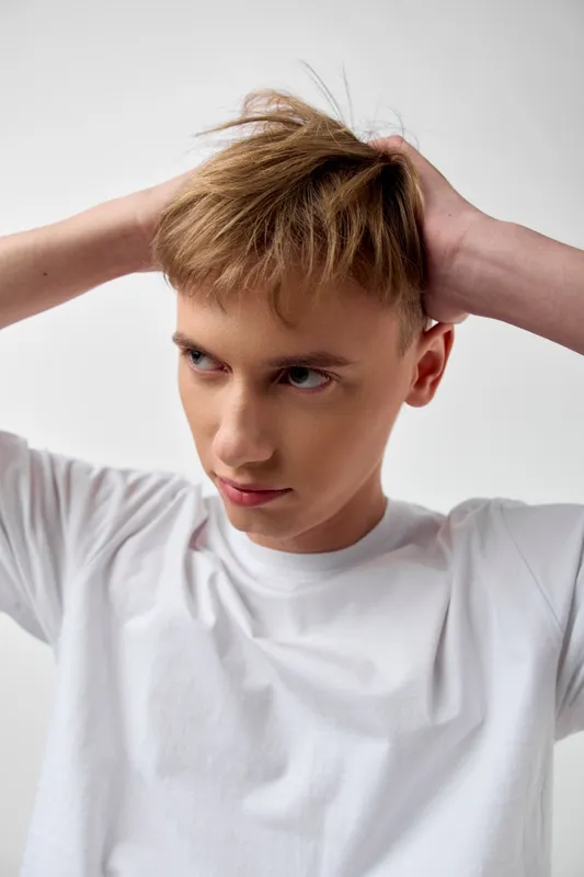 Hair, hairstyle, hands on head, expression of tension, white shirt, young adult, casual mood, grooming and fashion concepts in a studio setting for lifestyle and beauty campaigns