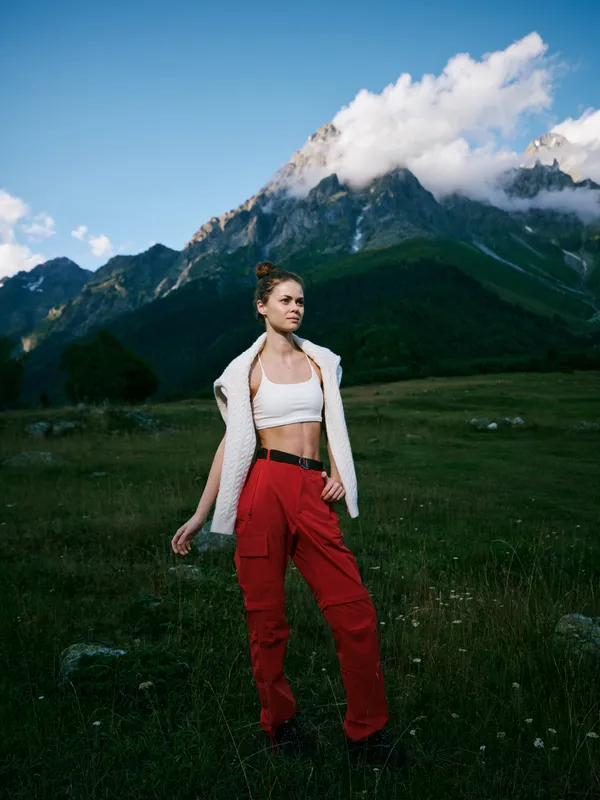 Fashion model stands in an alpine meadow under blue sky with towering mountains, showcasing outdoorwear and athletic style for nature, travel and adventure photography
