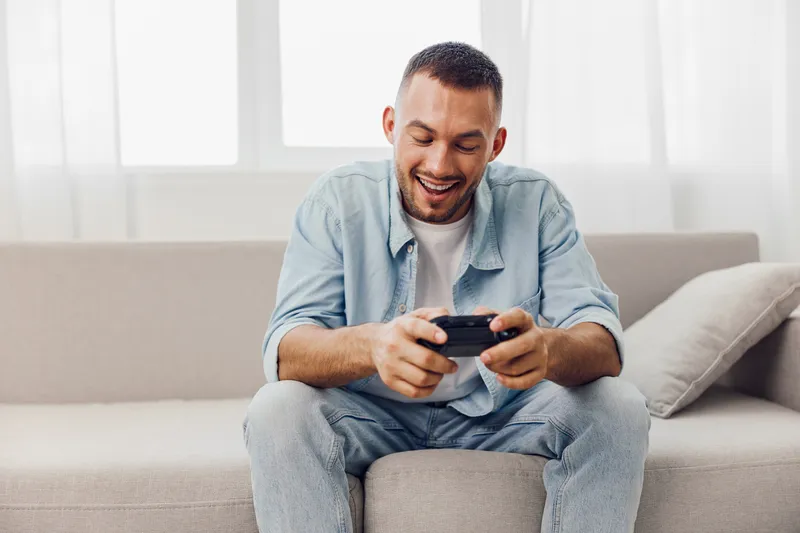 Smiling man enjoying a digital detox while playing video games, reflecting emotional minimalism and authentic imperfection in his home environment.