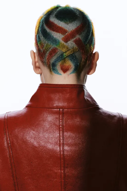 Artistic woman with colorful dyed short hair seen from behind wearing a textured red jacket, showcasing creative hairstyle and modern fashion style.
