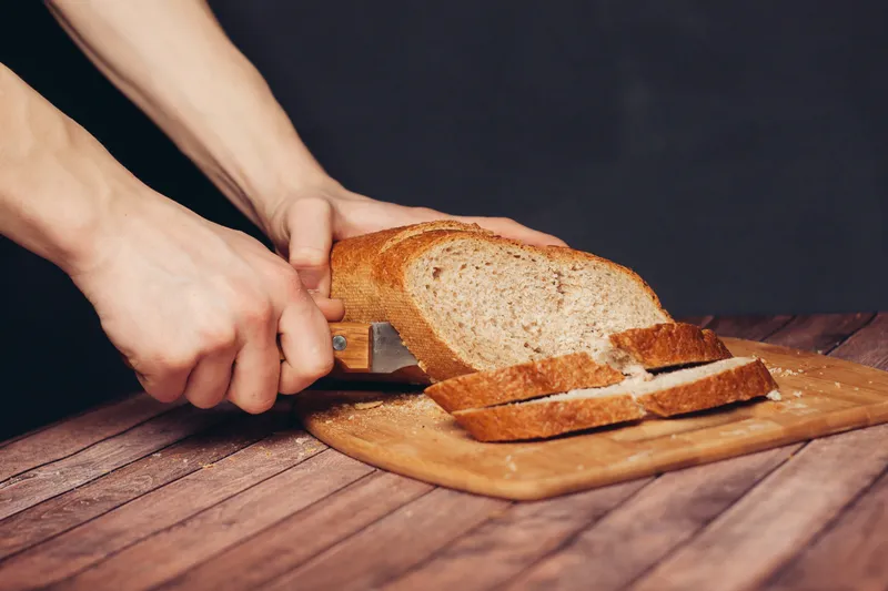 Нарезка буханки хлеба на разделочной доске, деревянный стол, кухня, еда, мука, продукт