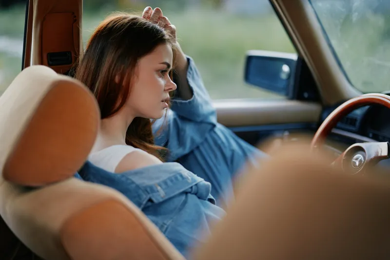 Young woman in a vintage car, wearing a denim jacket, contemplative expression, natural outdoor light, emphasizing relaxation, nostalgia, and wanderlust.