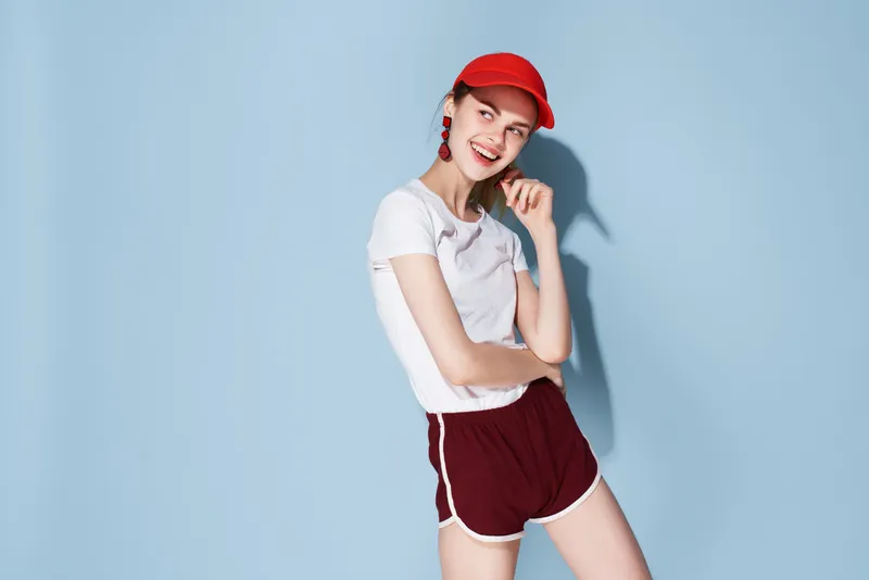 Женщина в красной кепке позирует в модной летней одежде, излучая веселье